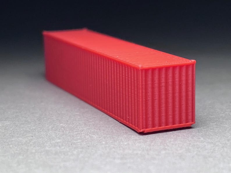 May include: A red shipping container model. The container is made of plastic and has a corrugated texture.