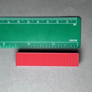May include: A red shipping container model measuring approximately 2 inches in length.