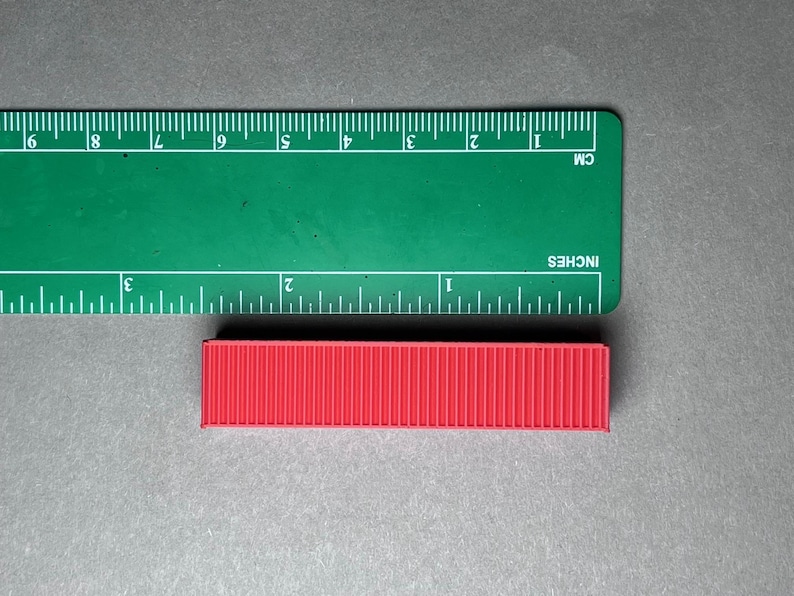 May include: A red shipping container model measuring approximately 2 inches in length.