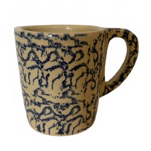 May include: A ceramic mug with a cream-colored base and a blue, abstract pattern. The mug has a rounded handle and a slightly flared rim. The design is reminiscent of traditional pottery.