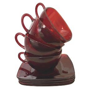 May include: A stack of ruby red glass teacups and saucers. The cups have rounded handles and sit atop square saucers. The set is made of transparent glass, and the color is consistent throughout the pieces. The cups and saucers are stacked neatly.