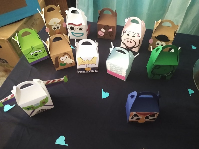 Puede incluir: Una colecci&oacute;n de cajas de regalo coloridas con temas de personajes, inspiradas en una popular pel&iacute;cula animada. Las cajas presentan varios personajes, con asas para facilitar el transporte. Las cajas est&aacute;n dispuestas sobre una superficie azul oscuro.