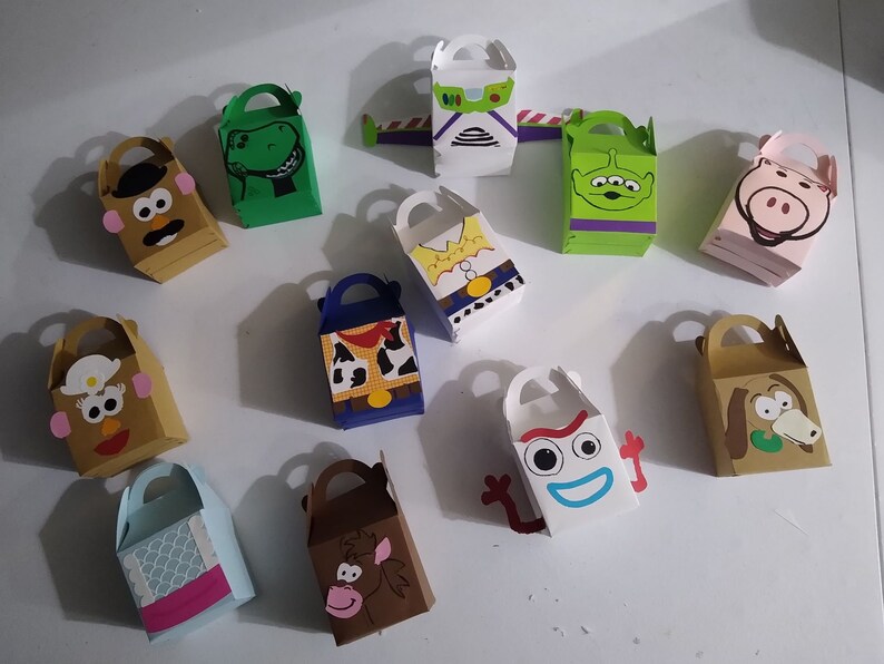 Puede incluir: Una colecci&oacute;n de cajas de regalo coloridas y hechas a mano con personajes de la pel&iacute;cula animada Toy Story. Las cajas son de varios colores y formas, con asas y caras de personajes como Sr. Cara de Papa, Rex y Buzz Lightyear.