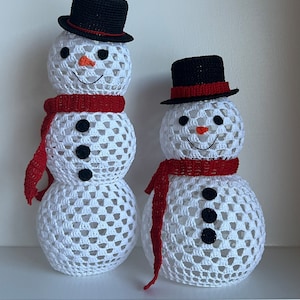 Puede incluir: Dos muñecos de nieve de crochet con sombreros negros y bufandas rojas. El muñeco de nieve más grande tiene tres botones negros y el más pequeño tiene dos.