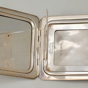 May include: A silver compact mirror with a hinged lid. The mirror is open, revealing a smaller mirror on the inside. The compact is engraved with the text "STERLING" and "Certified 925 Fine Silver".