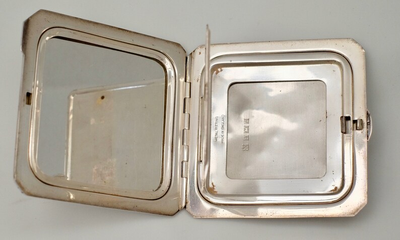May include: A silver compact mirror with a hinged lid. The mirror is open, revealing a smaller mirror on the inside. The compact is engraved with the text "STERLING" and "Certified 925 Fine Silver".