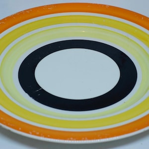 Op de afbeelding: Een rond keramiek bord met concentrische cirkels in oranje, geel en zwart. Het midden van het bord is wit.