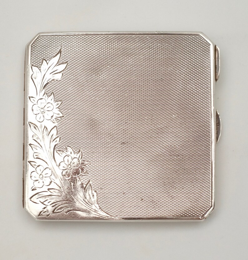May include: A silver cigarette case with a floral design engraved on the front.
