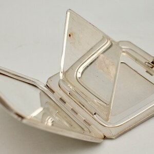 May include: A silver compact mirror with a hinged lid and two mirrors inside. The mirror is open and the lid is folded back.