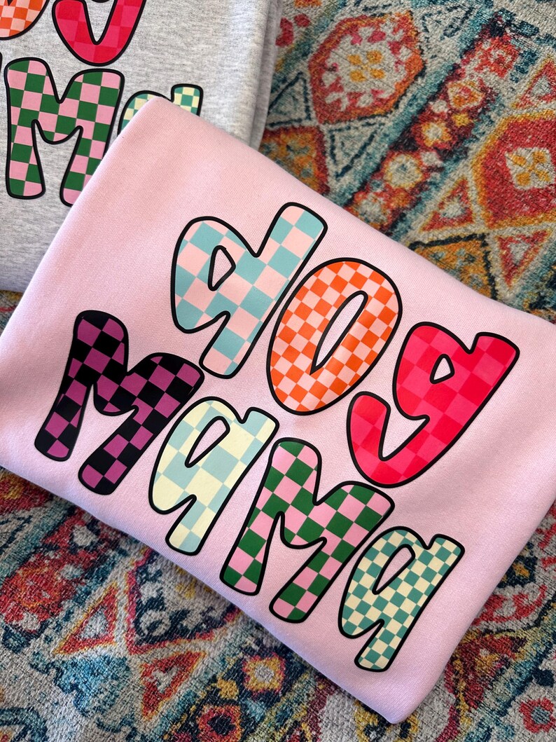 May include: Pink sweatshirt with the words "dog mama" in colorful checkered letters.