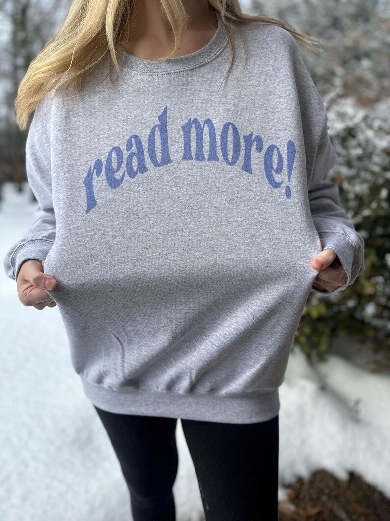 Puede incluir: Una sudadera gris con el texto "read more!" en letras azules.