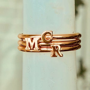 May include: Three gold-toned rings with the letters "M", "C", and "R" on them. The rings are stacked on top of each other.