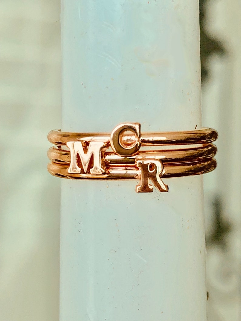 May include: Three gold-toned rings with the letters "M", "C", and "R" on them. The rings are stacked on top of each other.