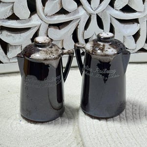 May include: Two dark brown ceramic pitchers with a glossy finish. Each pitcher has a handle and a lid with a white and brown speckled design. The text "Incline Railway Lookout Mtn., Tenn." is printed on the front of each pitcher.