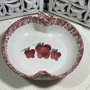 Puede incluir: Cuenco de cerámica blanco con forma de manzana con borde moteado rojo y blanco. El cuenco presenta un diseño pintado de tres manzanas rojas con hojas verdes. El cuenco está diseñado con forma de tallo y hoja en la parte superior.