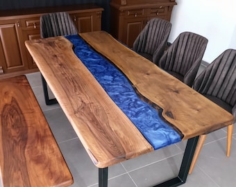May include: A wooden dining table with a blue resin inlay, a matching wooden bench, and four black upholstered chairs. The table and bench have black metal legs.