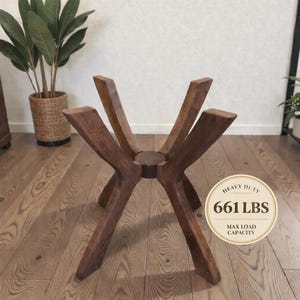 May include: A dark brown wooden table base featuring four angled legs connected at a central circular hub. A circular graphic overlay on the right side displays the text HEAVY DUTY 661 LBS MAX LOAD CAPACITY in black lettering on a cream background.