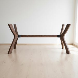 Puede incluir: Base de mesa de madera moderna con acabado marr&oacute;n oscuro. La base presenta un dise&ntilde;o &uacute;nico con patas anguladas y una viga de soporte horizontal. Las patas est&aacute;n conectadas con detalles met&aacute;licos negros. Adecuada para una mesa de comedor o de centro.