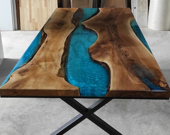 Puede incluir: Una mesa de madera con un río de resina azul que la atraviesa. La mesa tiene una base en forma de X de metal negro.