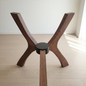 Puede incluir: Una base de mesa de madera con un dise&ntilde;o moderno y &uacute;nico. La base presenta cuatro patas anguladas en un acabado marr&oacute;n oscuro, conectadas por una pieza central circular negra. Las patas son de madera maciza y tienen un aspecto liso y pulido.