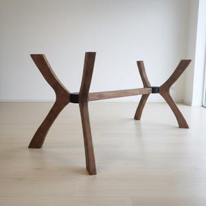 Puede incluir: Una base de mesa de madera con un dise&ntilde;o &uacute;nico y moderno. La base presenta cuatro patas anguladas conectadas por una viga horizontal. Las patas son de color marr&oacute;n oscuro y las uniones de conexi&oacute;n son negras. La base de la mesa est&aacute; dise&ntilde;ada para soportar una tapa de mesa.