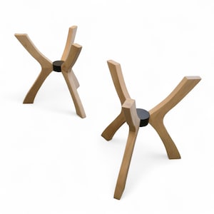 May include: Two wooden stands, each featuring four curved legs that extend outward from a central black circular hub. The light-toned wood has a smooth finish, and the structure is designed to provide a stable base for objects placed on top.