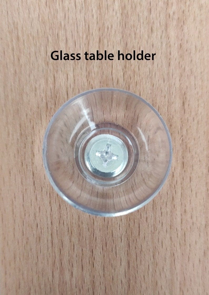 Puede incluir: Un soporte de mesa de vidrio transparente y circular con un tornillo met&aacute;lico en el centro. El texto "Glass table holder" est&aacute; impreso encima del soporte. El soporte est&aacute; sobre una superficie de madera marr&oacute;n claro.
