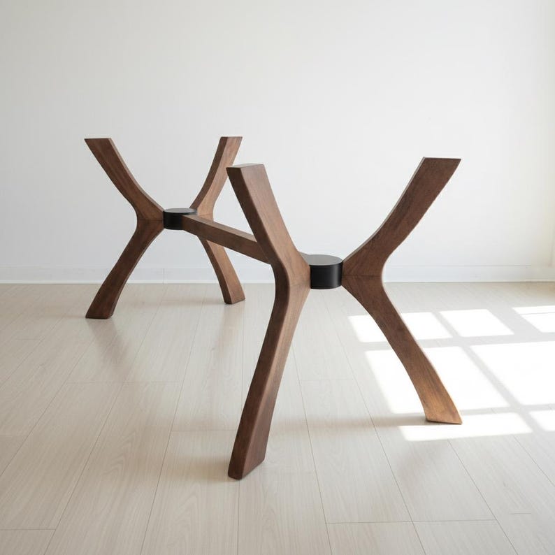 Puede incluir: Dos bases de mesa de madera con un dise&ntilde;o &uacute;nico y moderno. Las bases son de madera marr&oacute;n oscuro y presentan un dise&ntilde;o de patas curvadas en forma de X. Cada base tiene un conector circular negro en el centro. Las bases est&aacute;n sobre una pared blanca y un suelo claro.