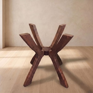 May include: A dark brown wooden table base featuring four angled, sturdy legs that extend outward from a central circular hub. The wood grain is visible throughout the structure, which is designed to support a tabletop surface above.