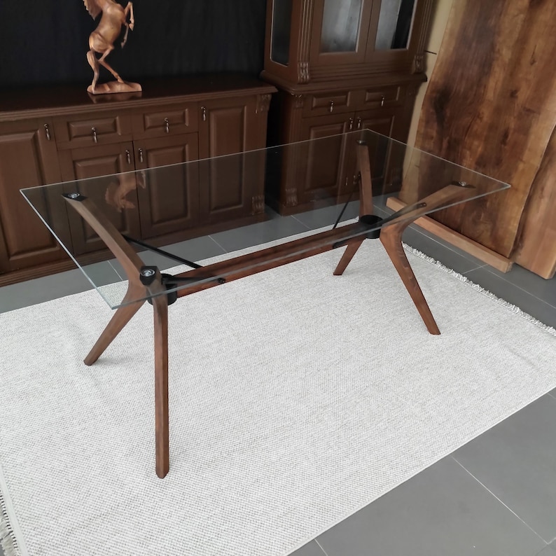 May include: A glass-top dining table with a walnut wood base. The table has a modern design with four legs that splay out from the center.