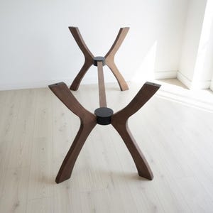 Puede incluir: Dos bases de mesa de madera con acabado marr&oacute;n oscuro. Cada base tiene cuatro patas curvas que se unen en el centro, conectadas por una viga de soporte central. Las patas est&aacute;n unidas con conectores circulares negros. Las bases est&aacute;n dise&ntilde;adas para una est&eacute;tica moderna.