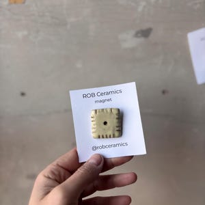 A yellow white cheddar cheez it refrigerator magnet is mounted on white cardstock and held in a hand