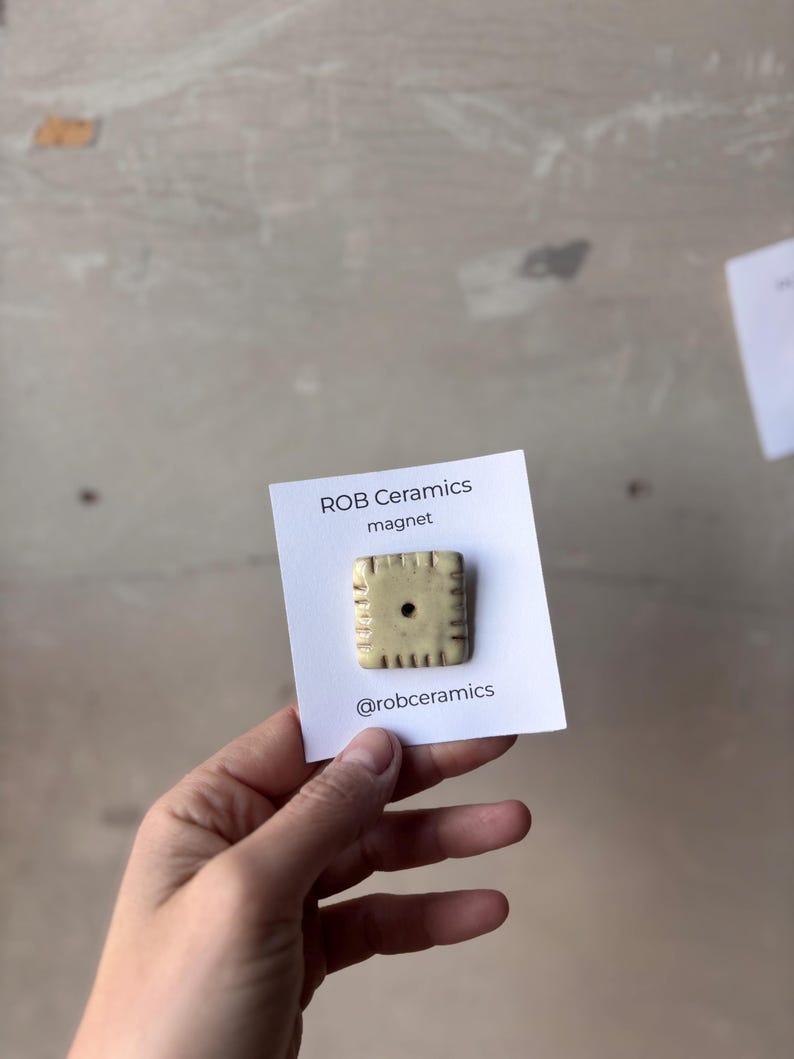 A yellow white cheddar cheez it refrigerator magnet is mounted on white cardstock and held in a hand