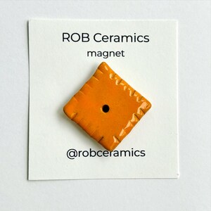 An orange cheez it refrigerator magnet is mounted on white cardstock