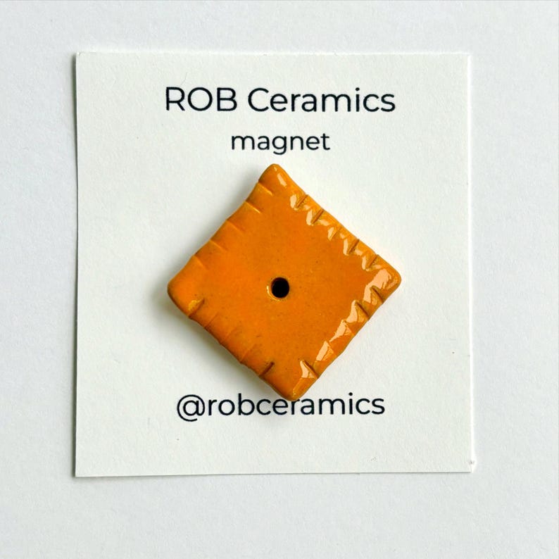 An orange cheez it refrigerator magnet is mounted on white cardstock
