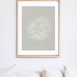 K&ouml;nnte beinhalten: Ein gerahmter Druck einer wei&szlig;en stilisierten Blume auf hellgrauem Hintergrund.