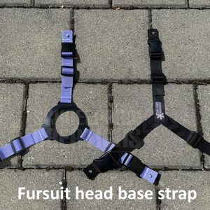 Könnte beinhalten: Zwei Kopfbasisgurte für Fellkostüme, einer lila und einer schwarz, mit verstellbaren Schnallen und einer runden Kopföffnung. Die Gurte liegen auf einer grauen Betonfläche. "Fursuit head base strap" steht in schwarzer Schrift am unteren Rand des Bildes.
