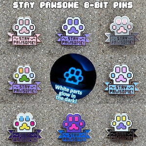 Könnte beinhalten: Neun 8-Bit-Pins mit Pfotenabdrücken und dem Text "Stay Pawsome!" auf einem Banner. Die weißen Teile der Pins leuchten im Dunkeln.