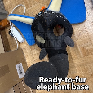 May include: A black and blue elephant base with the text "Ready-to-fur elephant base". The base has a black head with eye holes and a trunk. Blue wings are attached to the head.