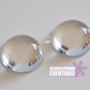 May include: Two clear glass cabochons, each with a slightly domed shape, are shown on a white surface.