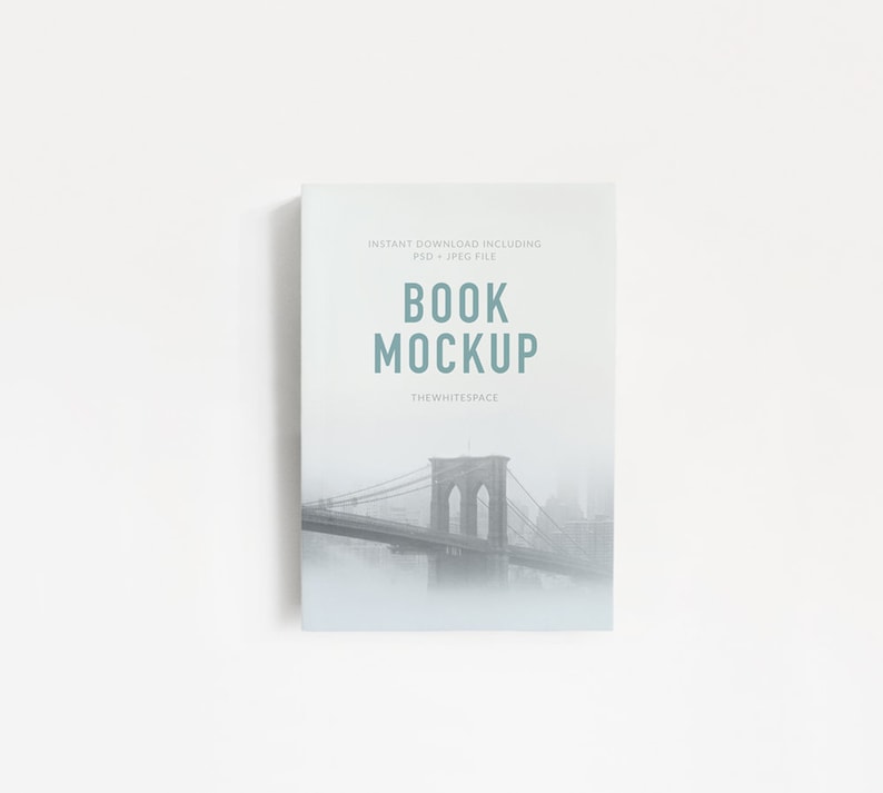 May include: A book mockup featuring a black and white photo of the Brooklyn Bridge in a foggy setting. The text on the cover reads "INSTANT DOWNLOAD INCLUDING PSD + JPEG FILE BOOK MOCKUP THEWHITESPACE".