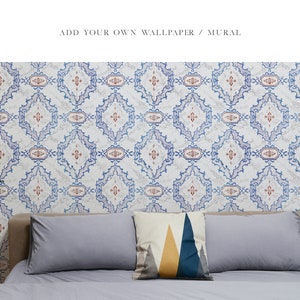 May include: A bedroom with patterned wallpaper featuring a blue and white geometric design. The wallpaper has a subtle red accent. A bed with grey linens and a geometric patterned pillow is in the foreground. A lamp with a white shade is on the left side of the image. A small wooden table with a white object on top is in the foreground.