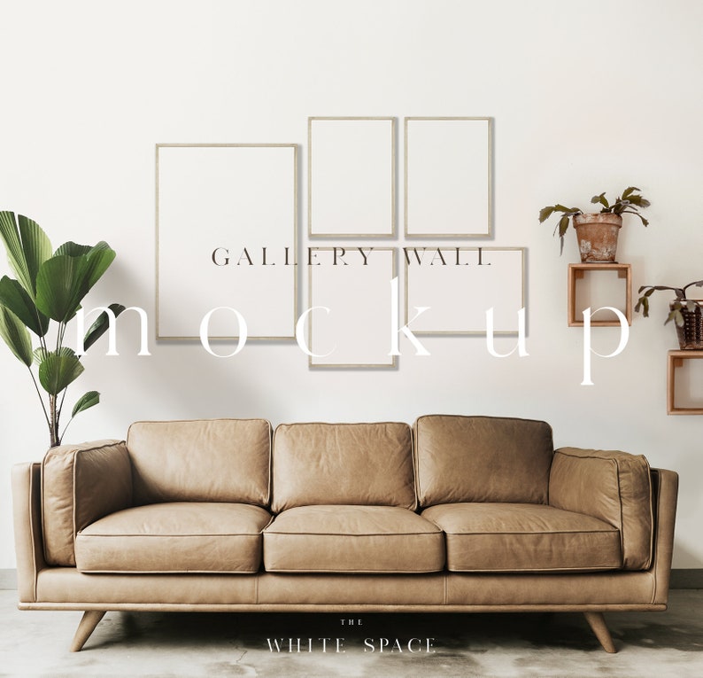 May include: A living room interior design mockup featuring a brown leather sofa with four empty picture frames on a white wall. The frames are arranged in a rectangular shape with the text "GALLERY WALL MOCKUP" printed below. The room is decorated with potted plants and wooden shelves.