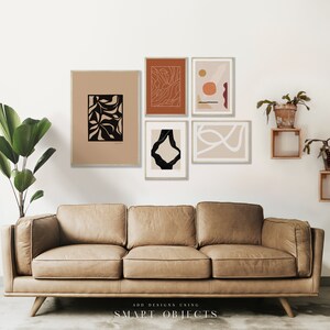 May include: Five abstract art prints in black, white, and orange frames, hanging on a white wall above a brown leather sofa. The prints feature geometric shapes, lines, and organic forms.