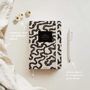 May include: A black and white journal with a patterned cover featuring a maze-like design. The cover also has the text "MY JOURNAL" in a black rectangle. The journal is lying flat on a white surface.