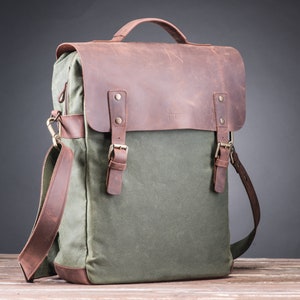 May include: A green canvas and brown leather backpack with a top handle and adjustable shoulder strap. The bag has two buckles on the front and a zipper closure.