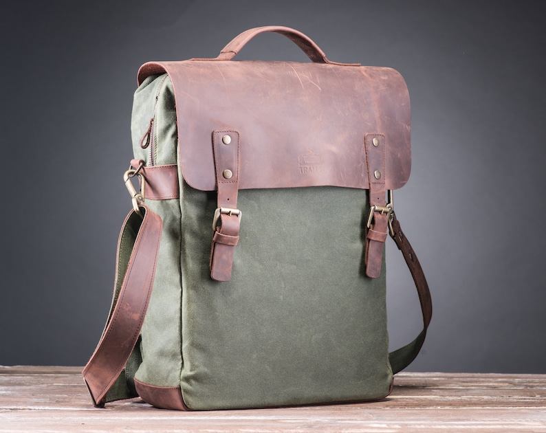 May include: A green canvas and brown leather backpack with a top handle and adjustable shoulder strap. The bag has two buckles on the front and a zipper closure.