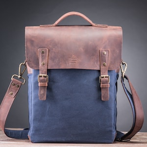May include: A brown leather and blue canvas messenger bag with a flap closure and two buckles. The bag has a long adjustable strap and a small logo that says "TRAM 21".