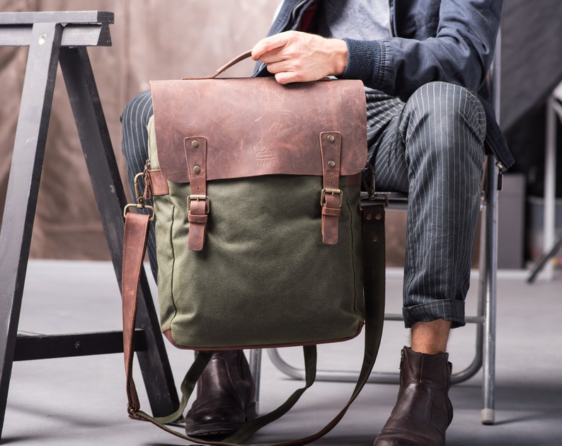 May include: A green canvas and brown leather messenger bag with adjustable shoulder strap and buckle closures.