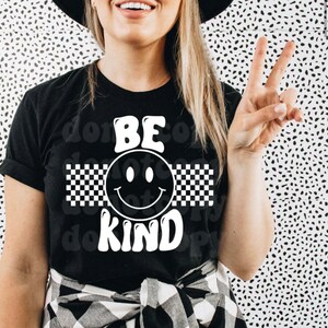 May include: Black t-shirt with a white smiley face and checkered pattern. The text "BE KIND" is written in white letters.